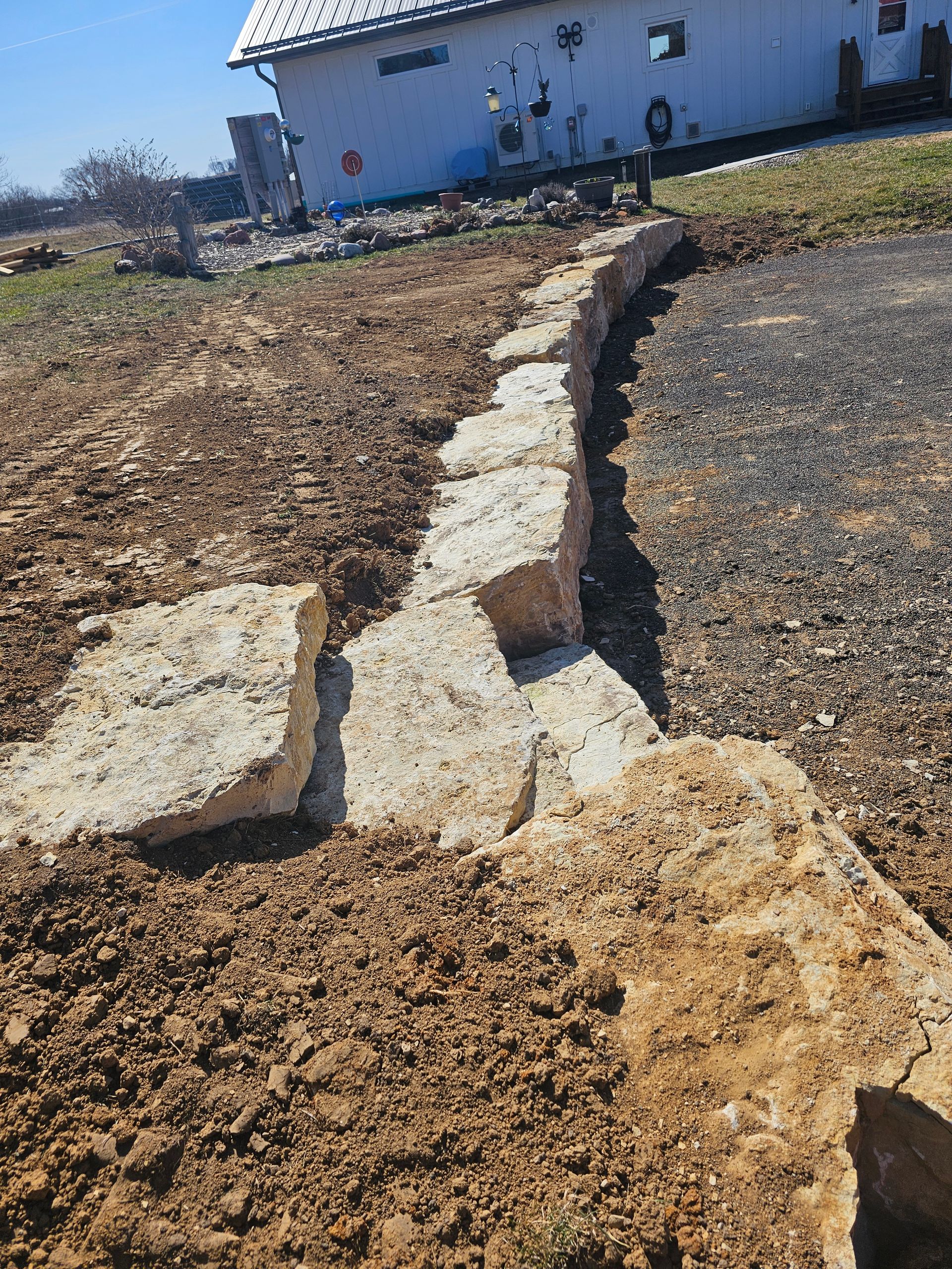 A stone wall is being built in a dirt field in front of a house.
