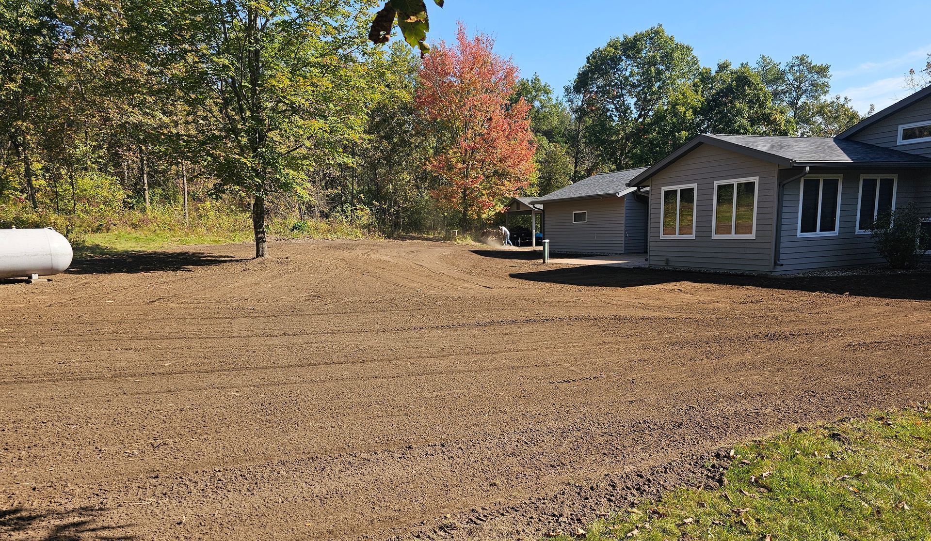 A house is sitting in the middle of a dirt field next to a propane tank.