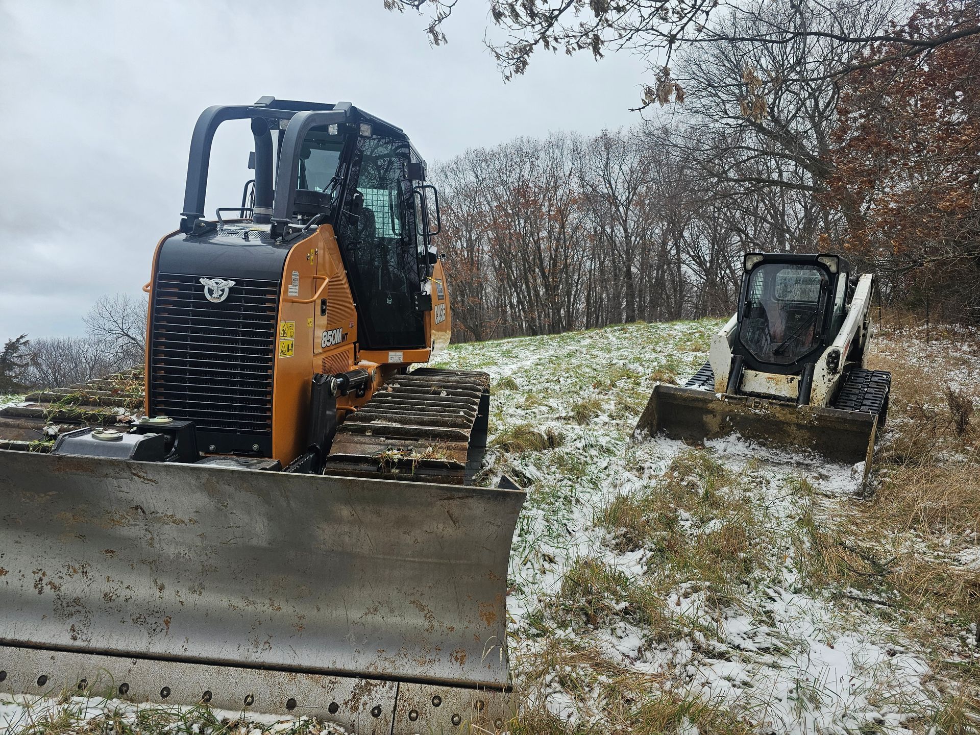 Two bulldozers are parked in a snowy field.