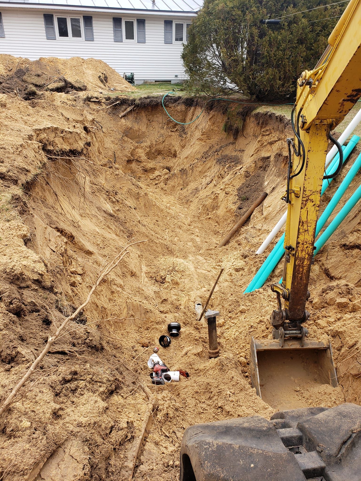 A yellow excavator is digging a hole in the dirt in front of a house.