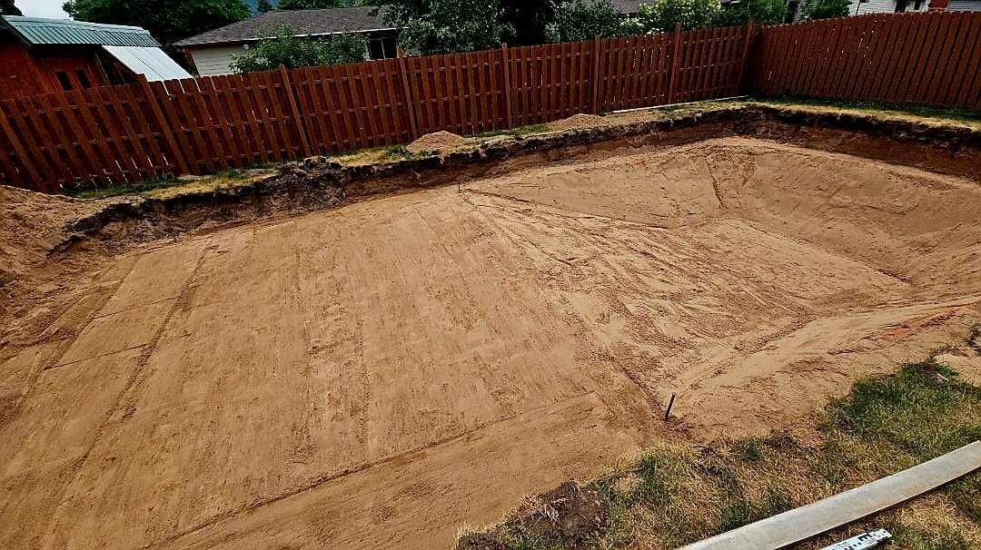 A large pile of dirt in a backyard next to a wooden fence.