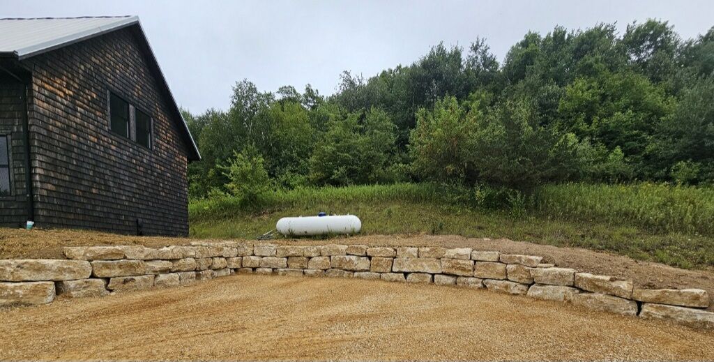 A house is sitting in the middle of a field next to a stone wall.