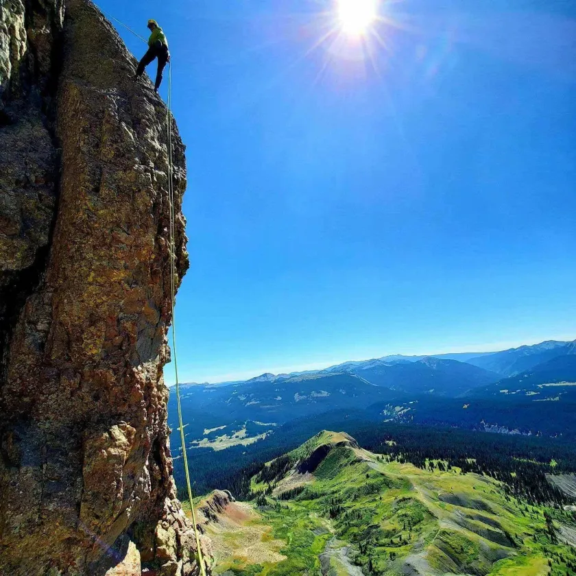 Rock climber on cliff with view of the San Juan Mountains outside of Durango.