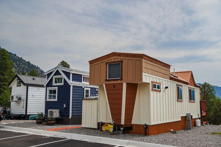 Three tiny houses of different colors parked outdoors. The center house has a brown facade.