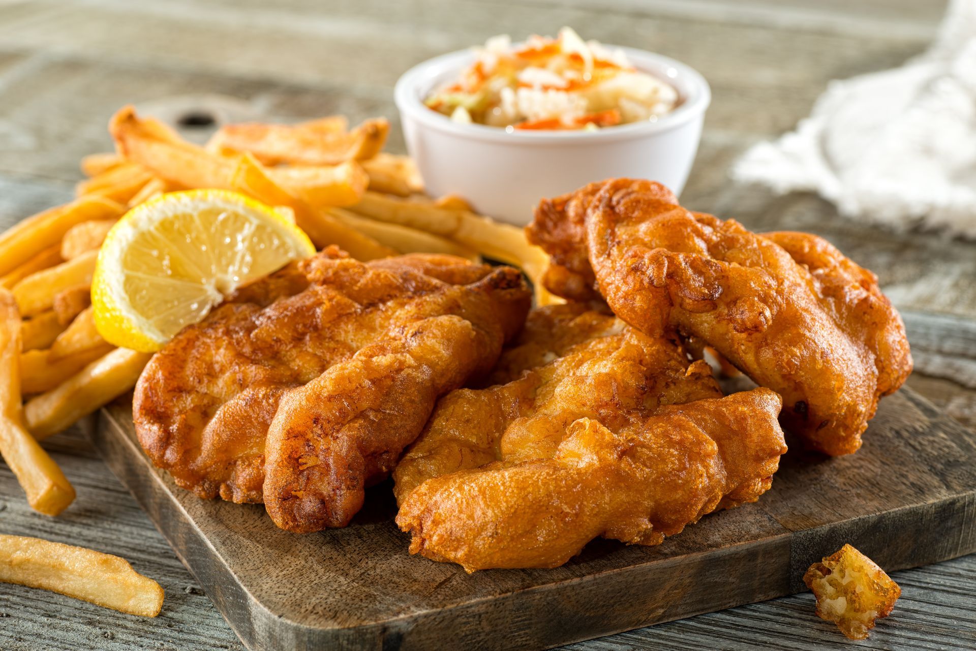 A wooden cutting board topped with fried fish and french fries.