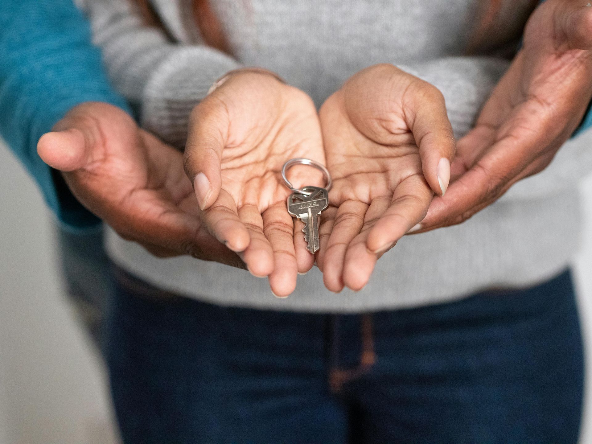 Hands holding keys, another pair of hands gently supporting underneath.