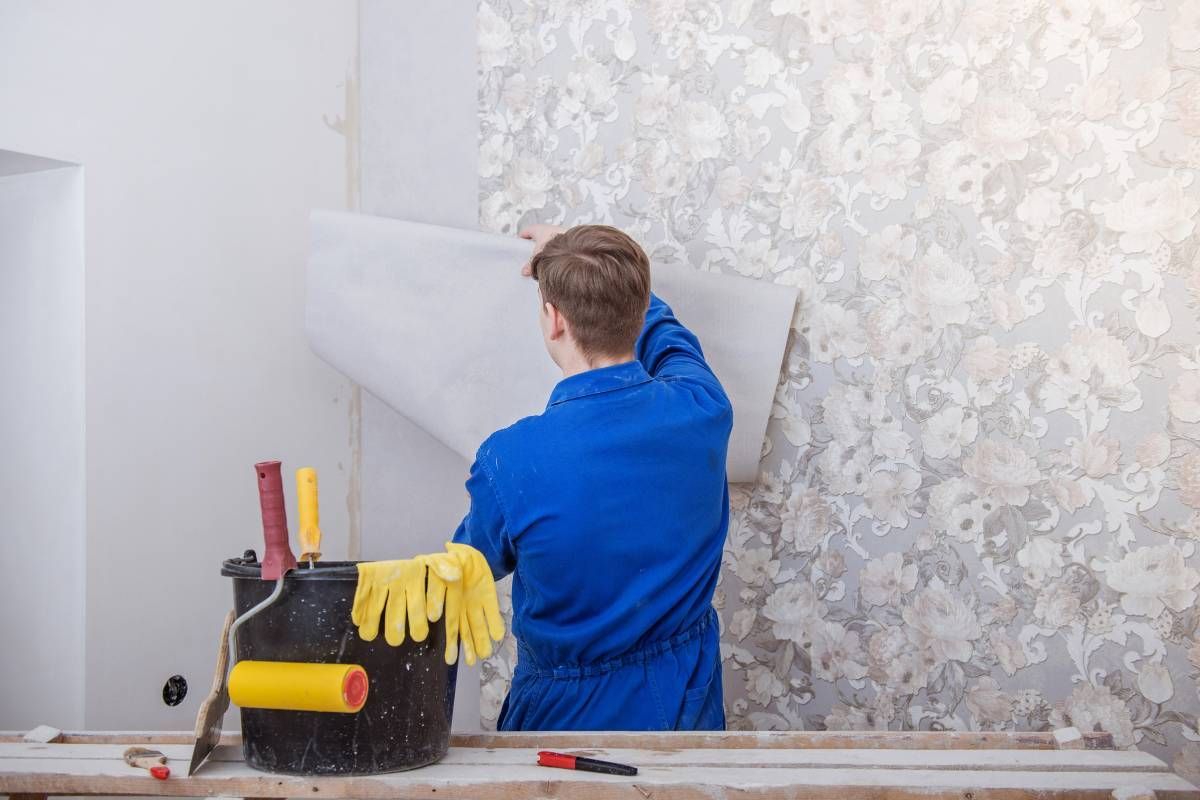 A professional installer applying custom floral wallpaper to a home's interior wall with careful precision near Vestal, NY