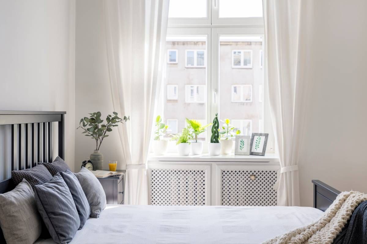 White custom drapes on a bedroom window with a cozy bed and plants decorating the space Vestal, NY