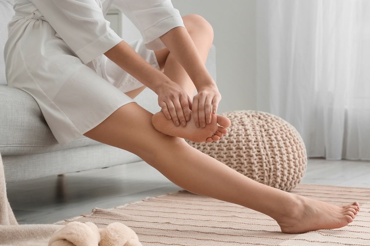 Woman sitting on sofa and making foot massage in room, closeup