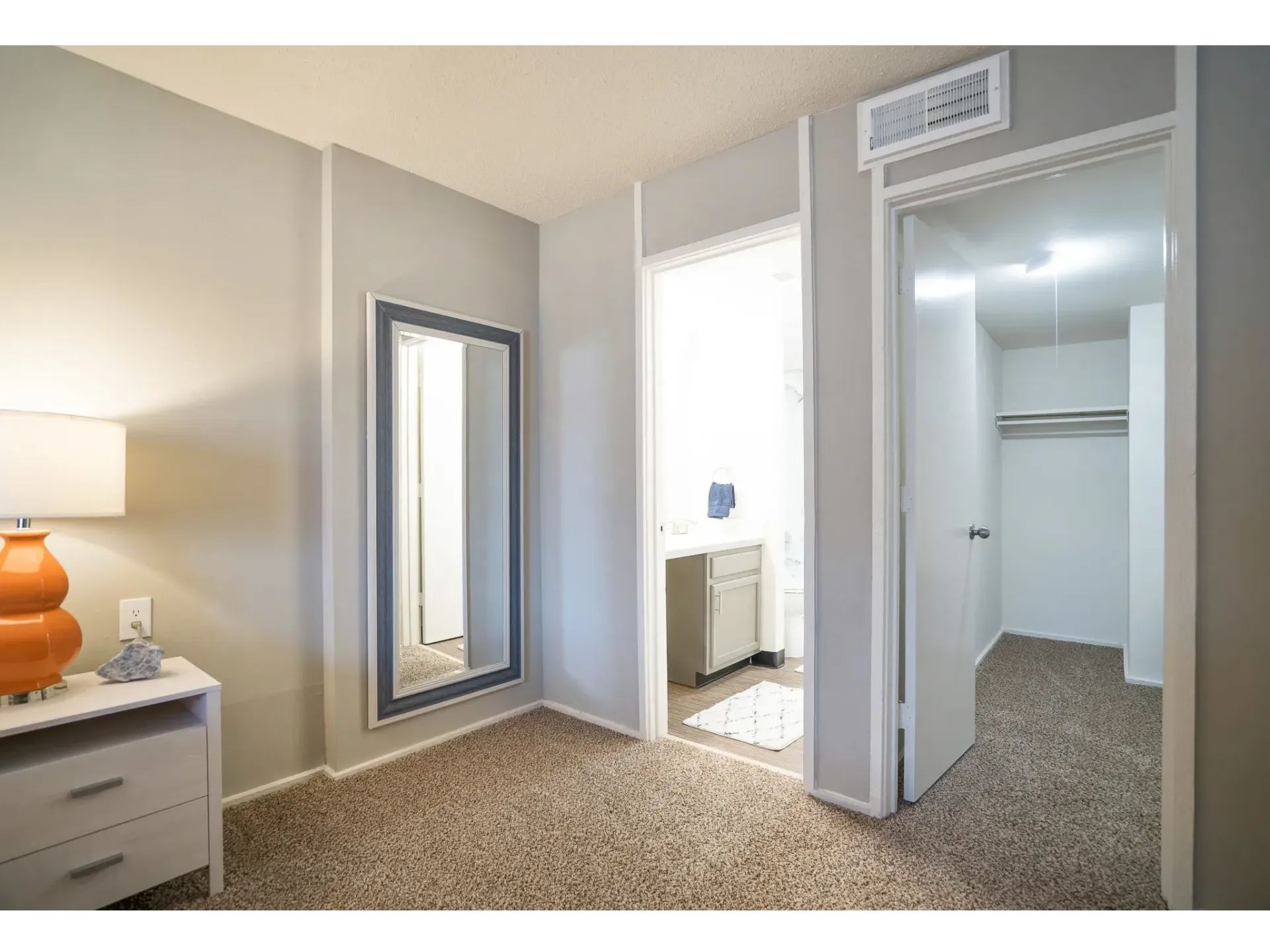 A well-lit apartment interior showing a bedroom with a decorative lamp and a mirror.