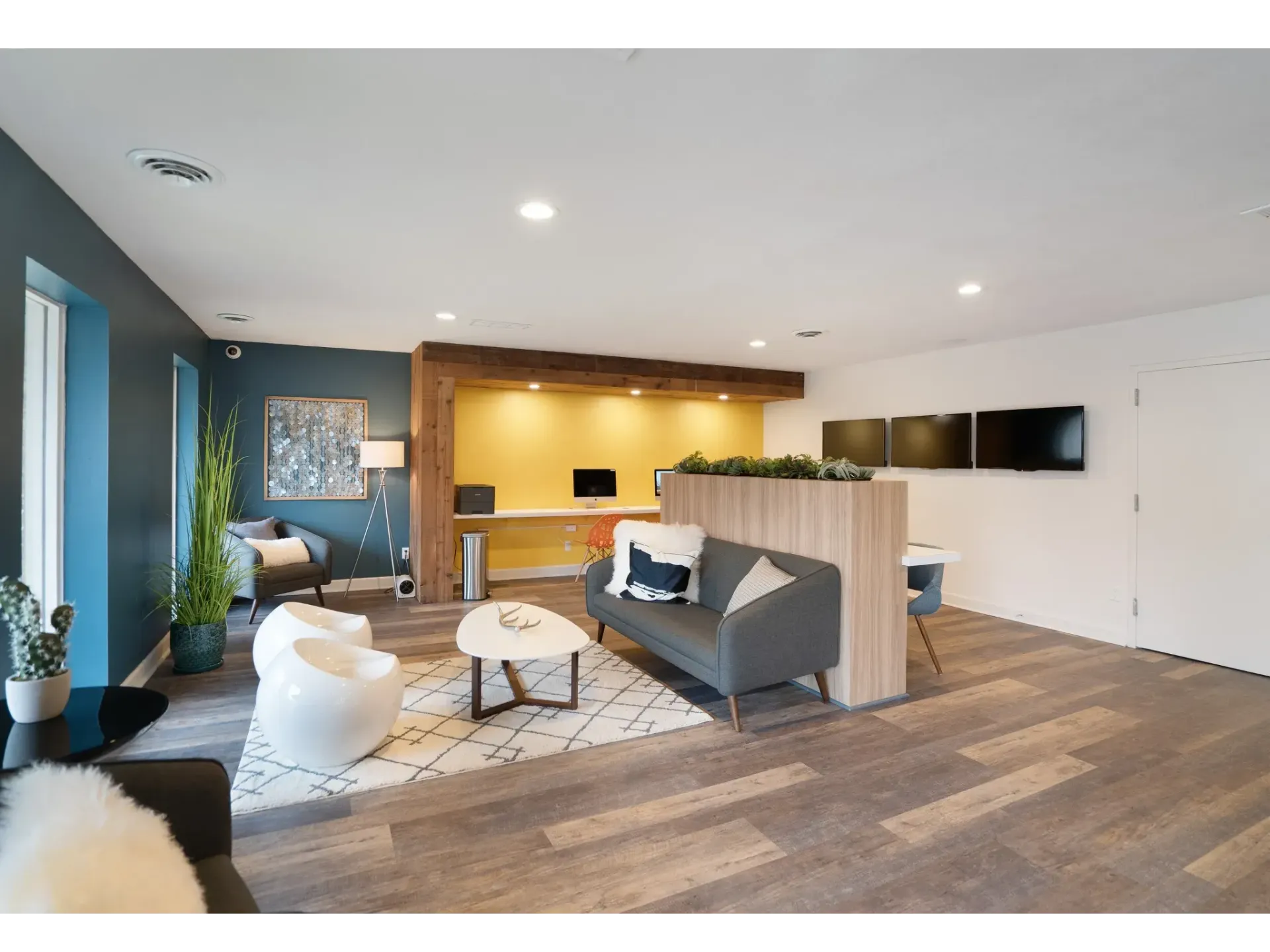 A modern lounge area with seating, plants, and a desk.