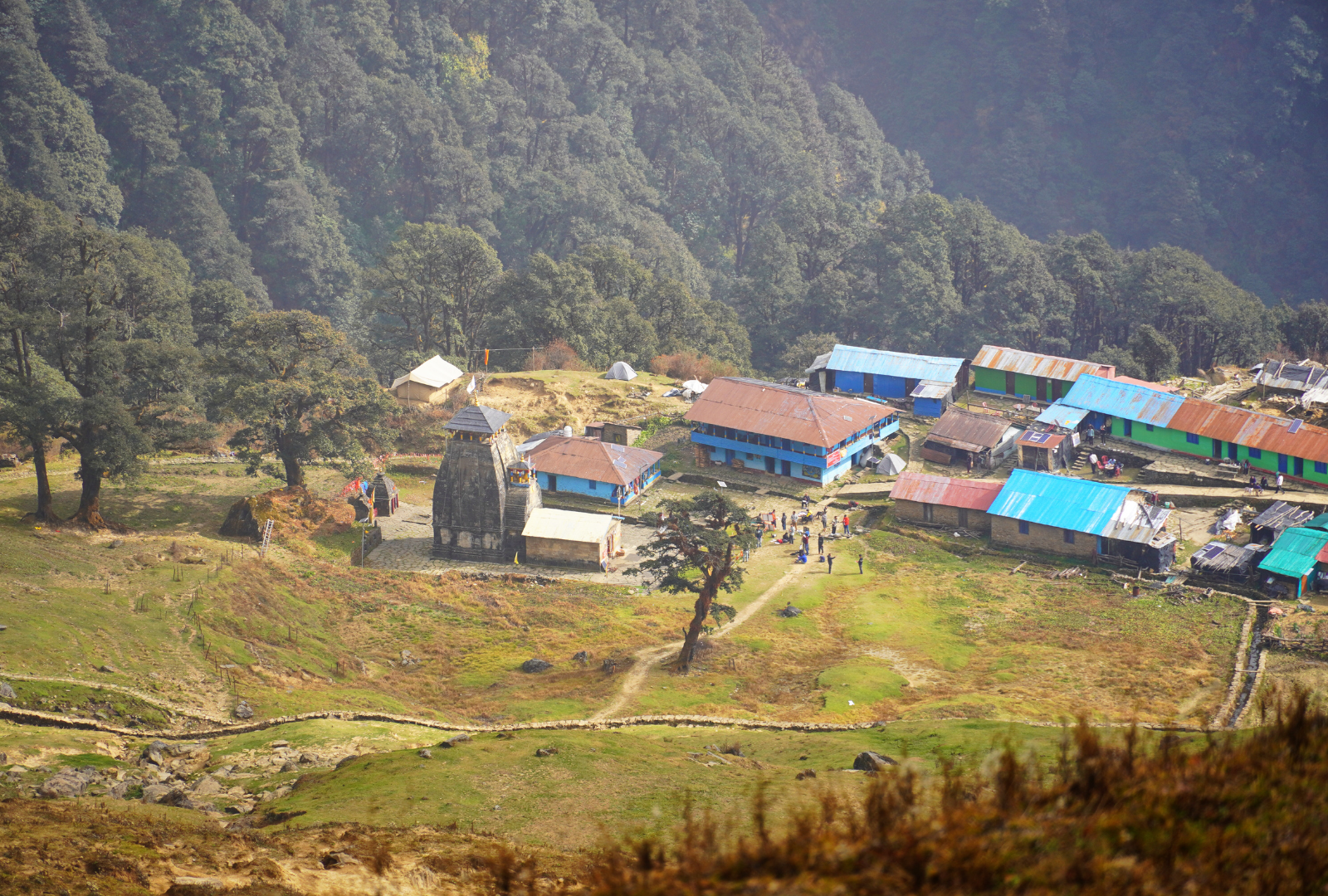 Village nestled in a mountain valley, with buildings and a temple, surrounded by trees and green hills.