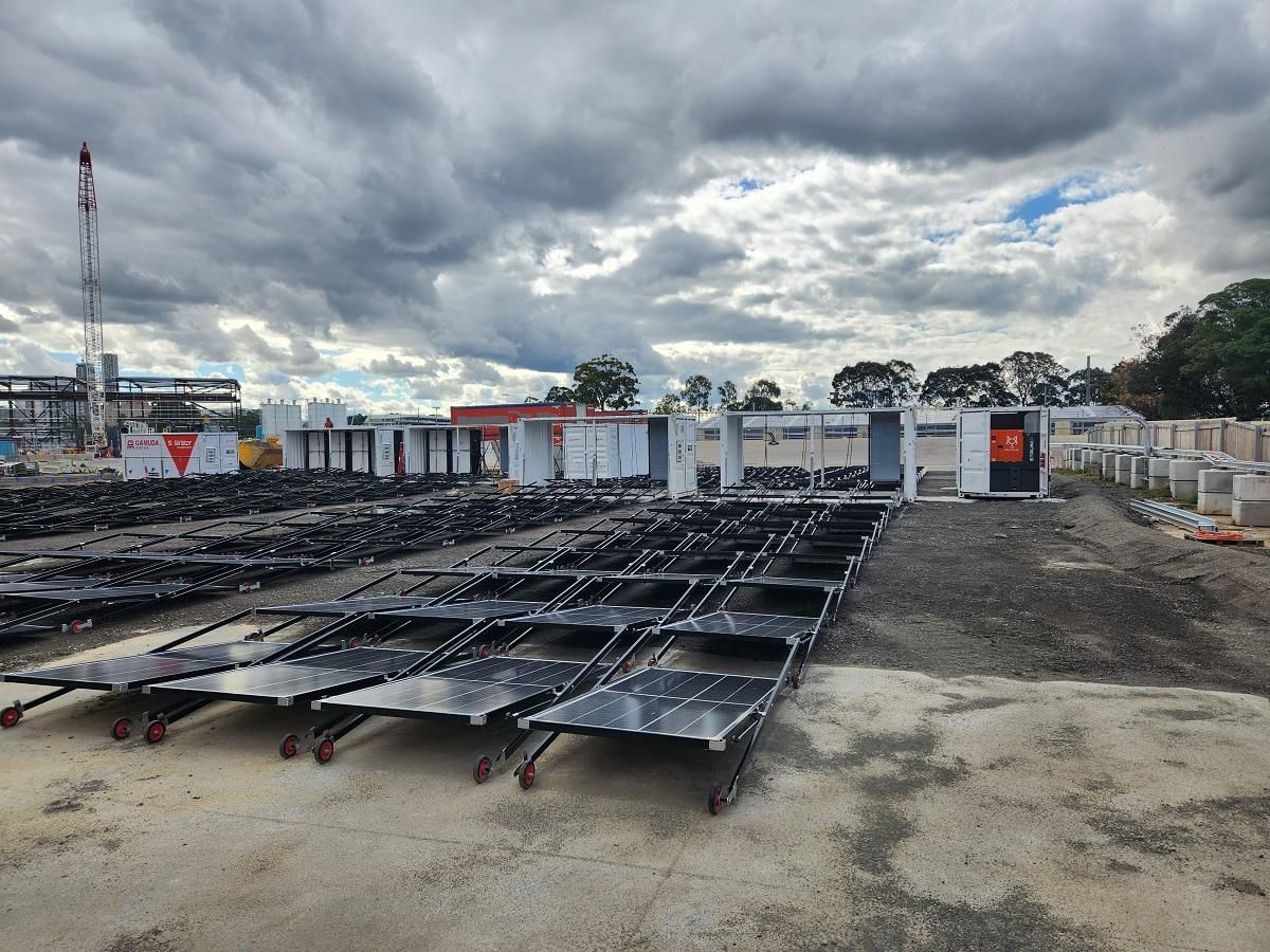 Black solar panels and white modular buildings under a cloudy sky at an outdoor construction site.