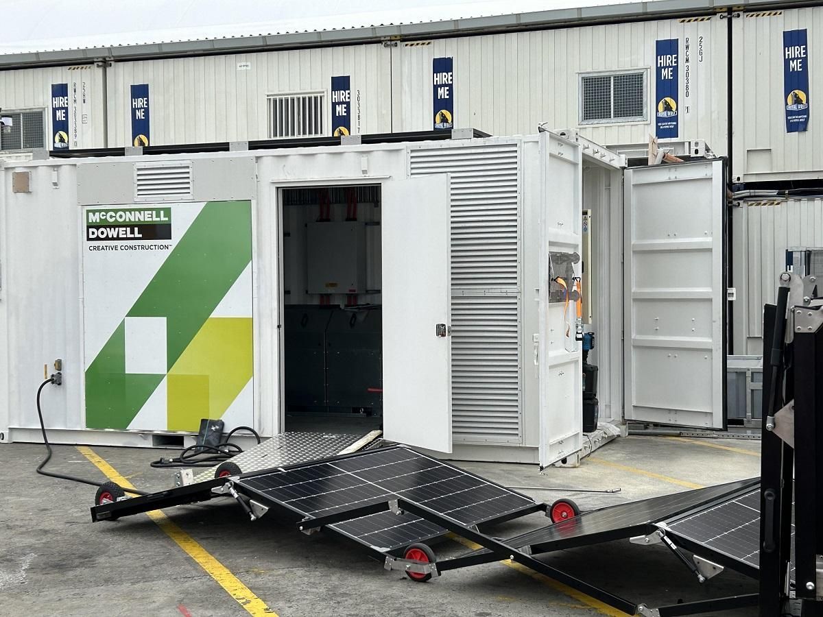 Mobile solar panel array deploying from a white container. The container has a door open, revealing interior equipment.
