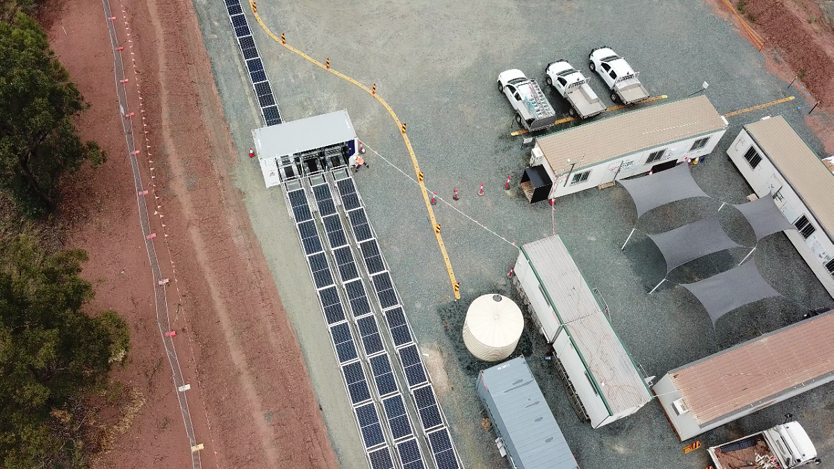 Overhead view of a solar panel array powering a construction or work site with buildings, vehicles and equipment.