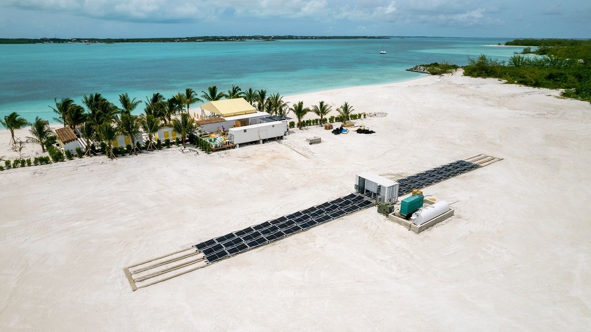 Aerial view of a white sandy beach with turquoise water. Buildings and seating are set up. Trees border the beach.