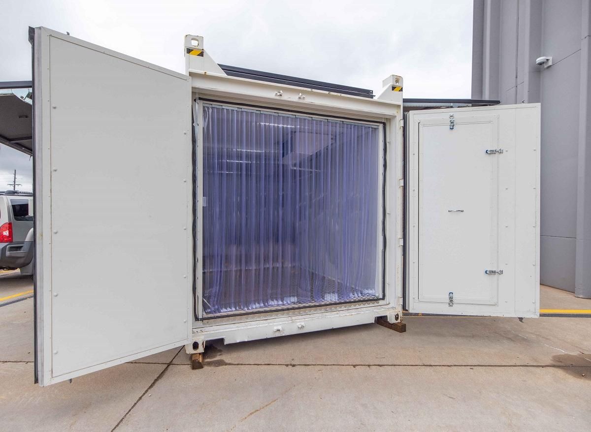 White shipping container with open doors, plastic strip curtains inside.