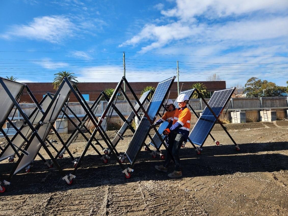Two workers installing foldable solar panels outdoors on a sunny day.