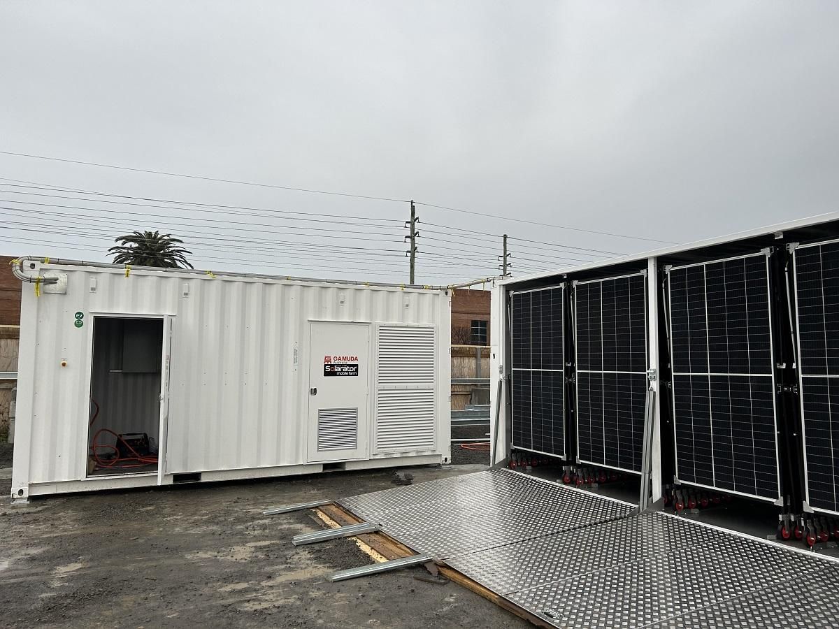 White container with open doors next to solar panels and a metal platform, set against an overcast sky.