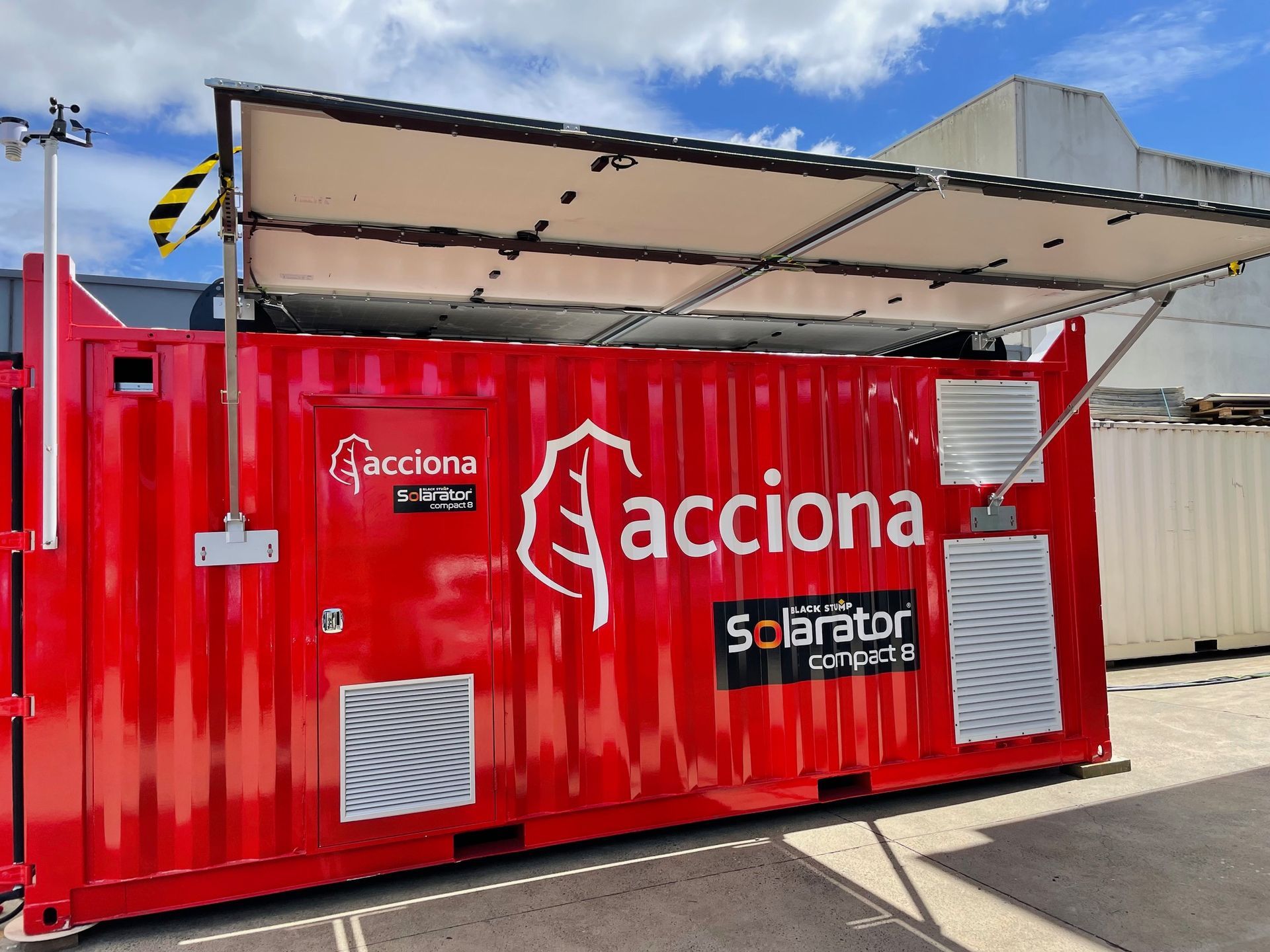 Red "Acciona Solarator" container with solar panels, likely used for power generation, outdoors.