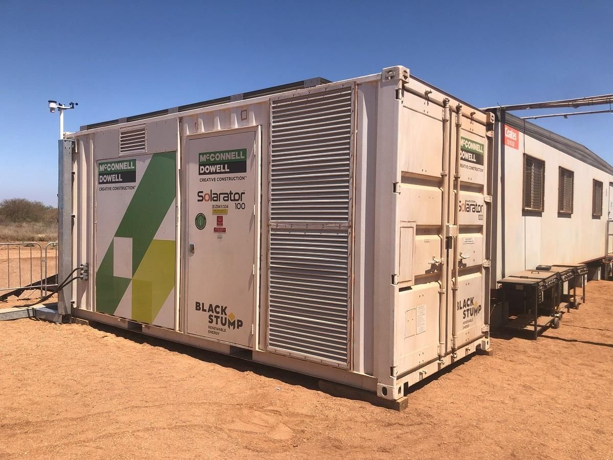 White shipping container with green and yellow accents, beside a mobile office trailer, outdoors.