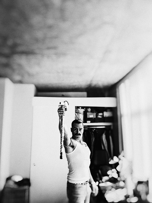 Man in a tank top holds up object in room with open closet.