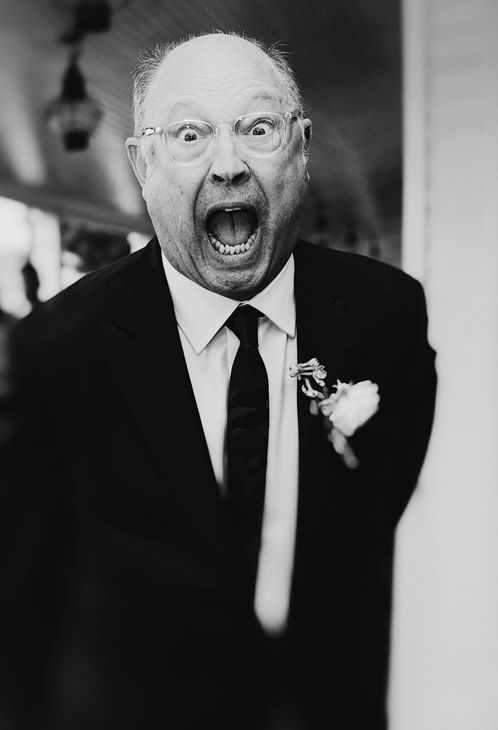 Man in suit with open mouth, shocked expression; standing indoors.