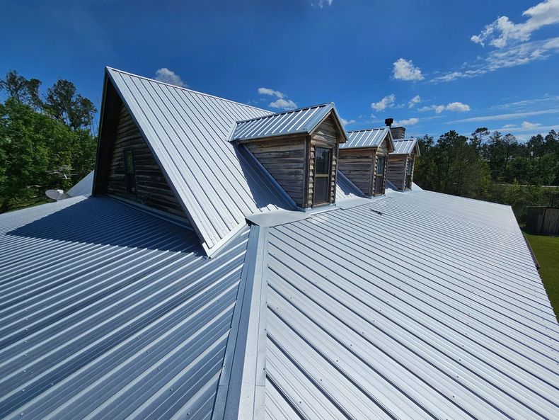 White metal roof on a house with two dormers under a bright blue sky