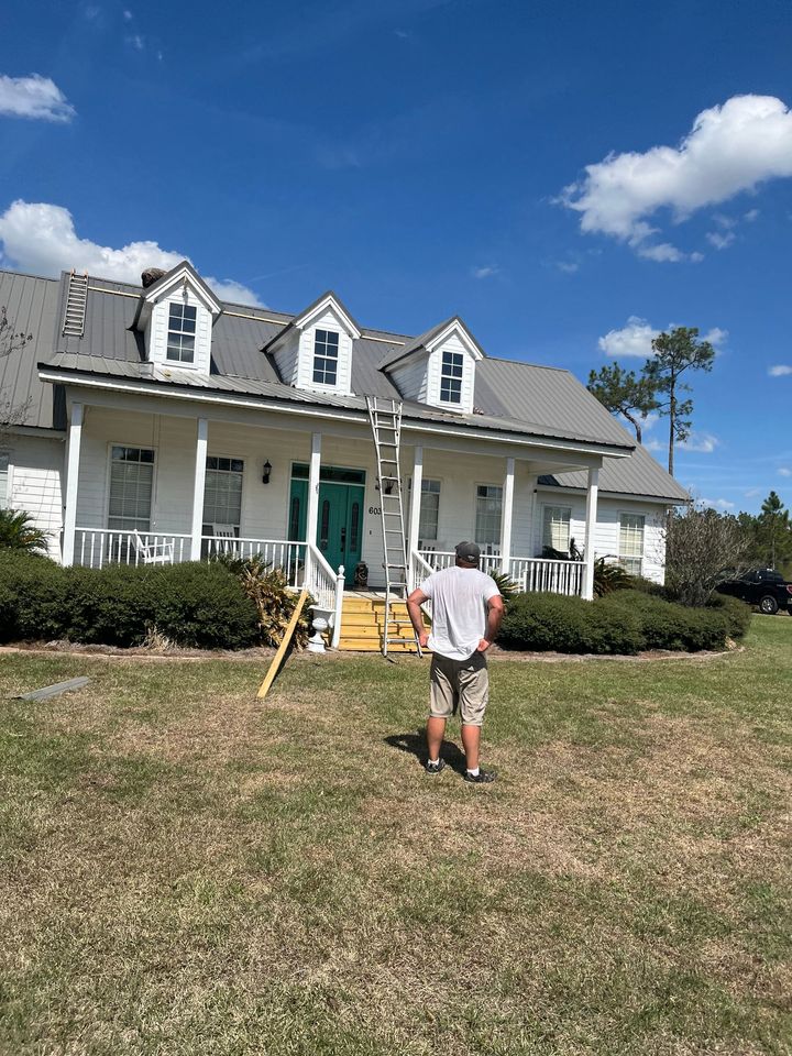 White farmhouse with dormer windows and porch, a person standing on a grassy lawn under a blue sky.