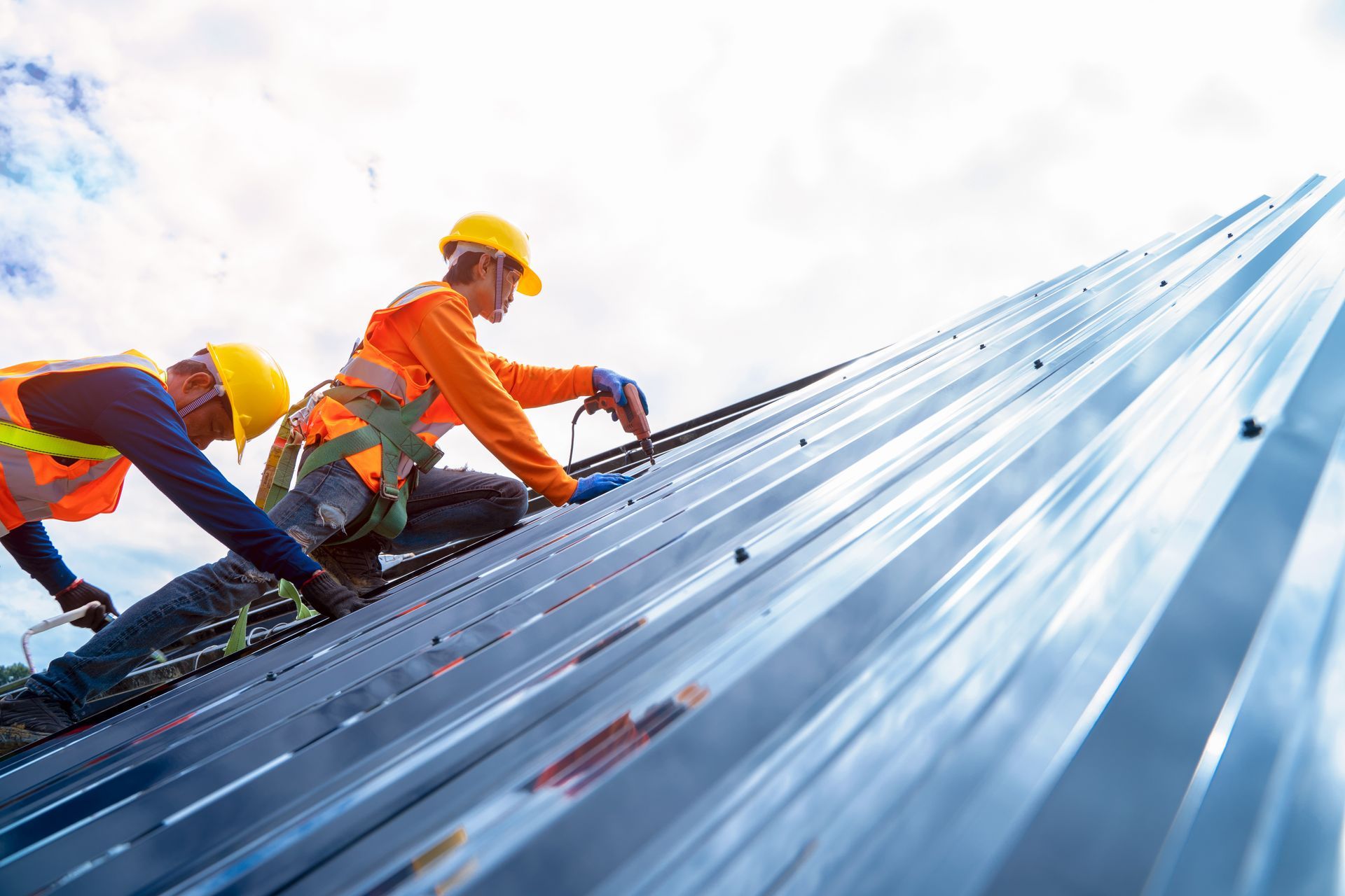 Two construction workers in safety gear installing a metal roof on a steep slope