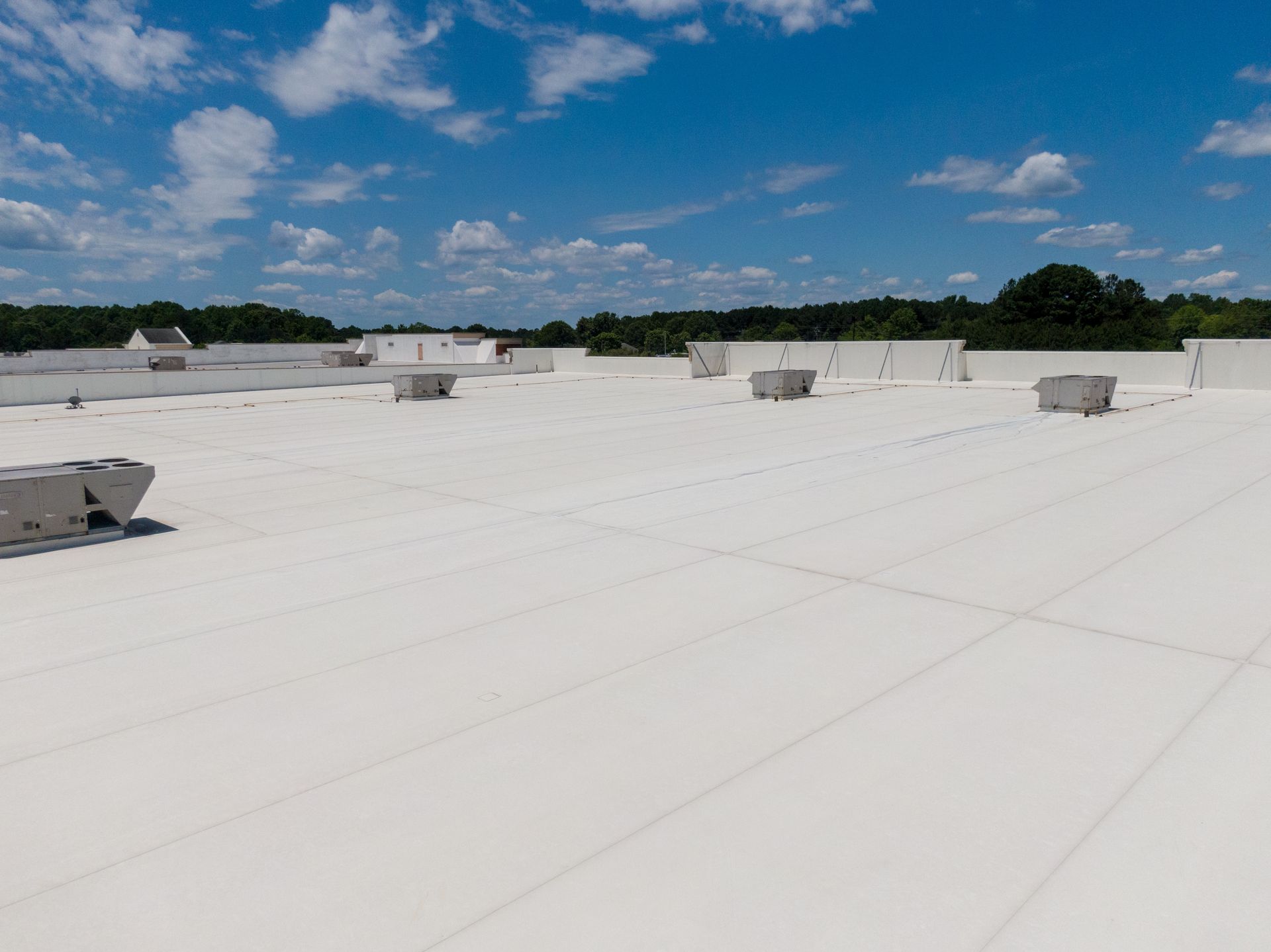 White commercial rooftop under a blue sky with scattered clouds and small rooftop units