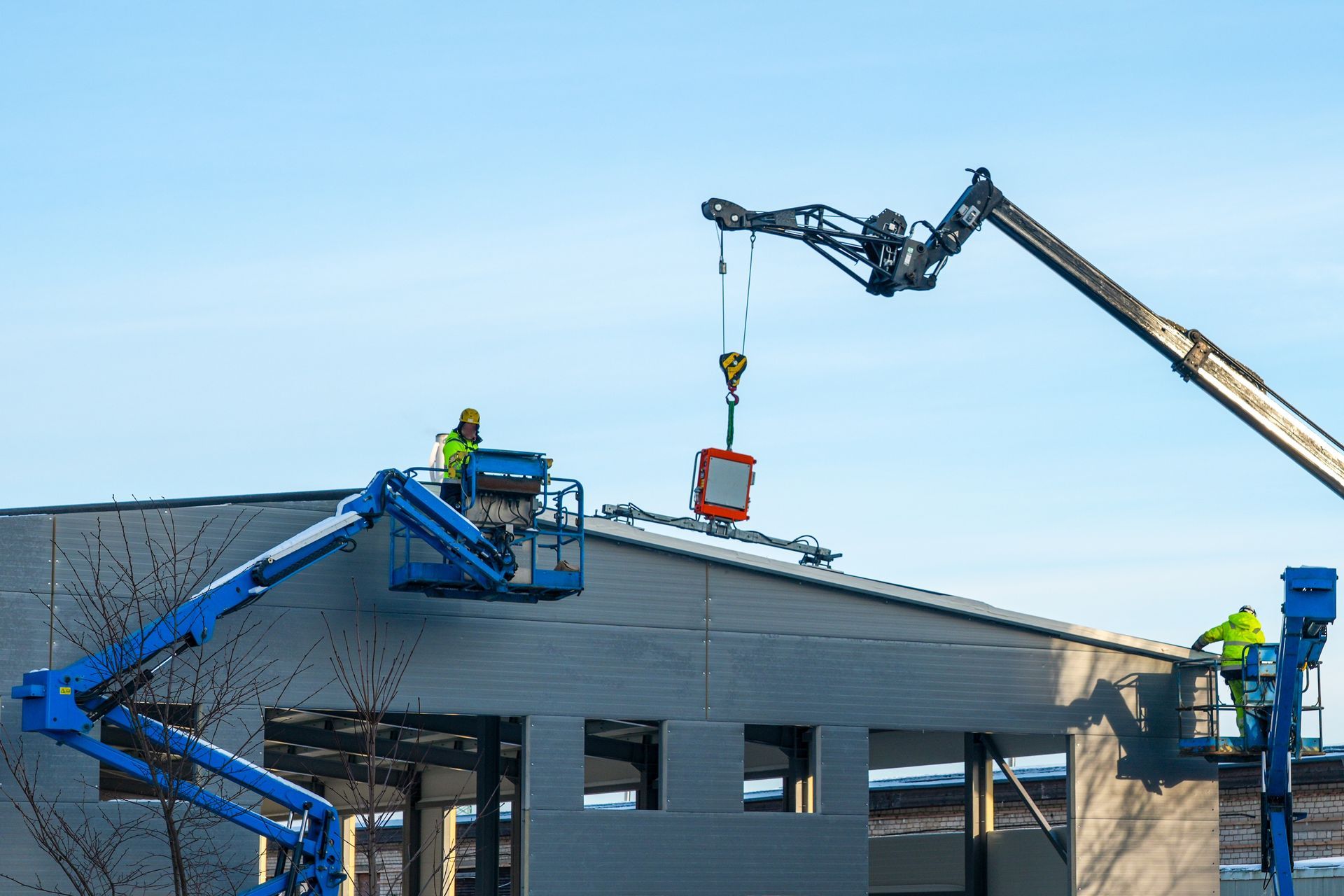 Workers on lifts installing rooftop equipment on a building under construction