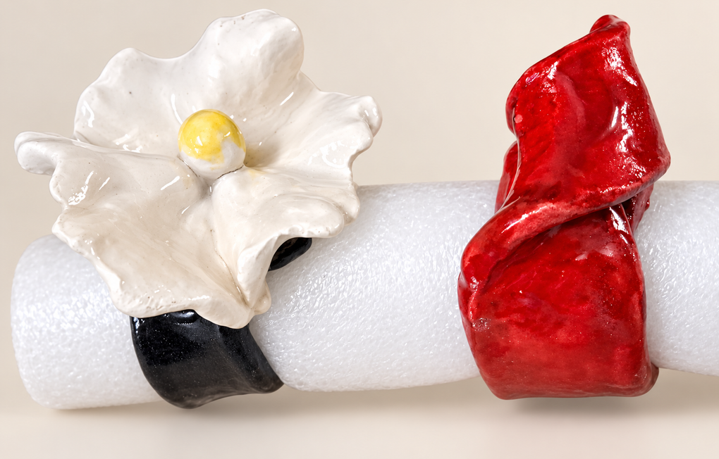Due anelli decorativi, uno con un fiore bianco e una fascia nera e l’altro con una fascia rossa a forma di nastro, su una superficie bianca
