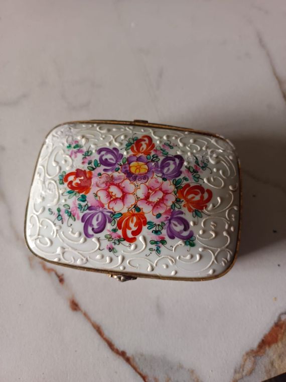 Piccola scatola d’argento con incisioni floreali e fiori dipinti a colori, su una superficie di marmo