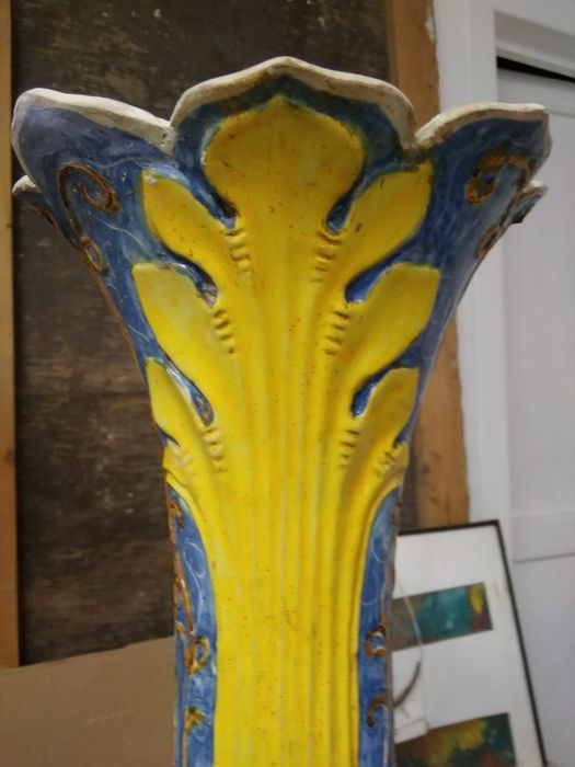 Primo piano di un vaso decorativo in ceramica giallo e blu o della sommità di una colonna, con motivi a foglie