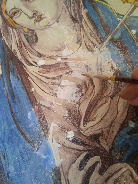 Primo piano di una figura dipinta nei toni del blu e del beige, con una mano che regge un pennello