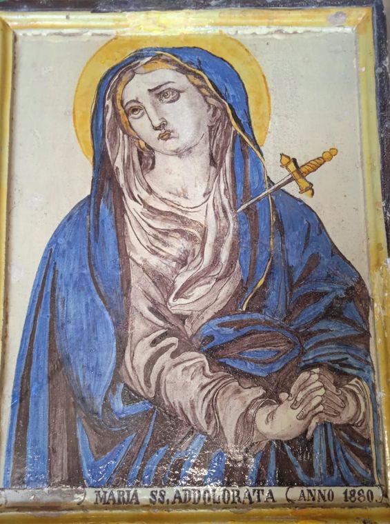Santo con aureola, vestito di blu, con le mani giunte e un’espressione solenne, che regge un bastone a forma di croce