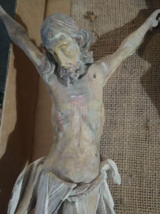 Scultura di Gesù crocifisso con le braccia distese, consumata e sbiadita, su uno sfondo intrecciato