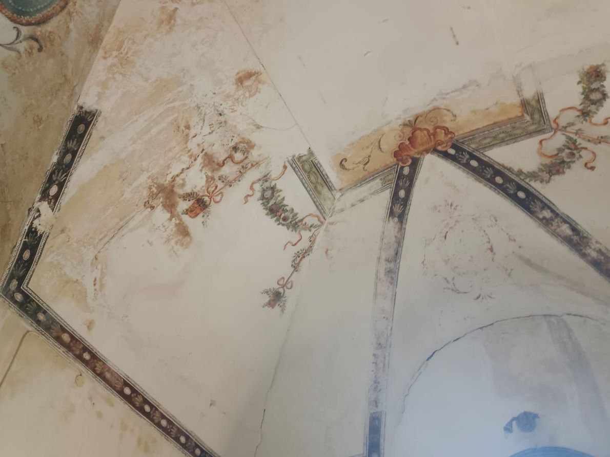 Soffitto danneggiato, con vernice scrostata, macchie e supporti metallici a vista, ripreso in un angolo