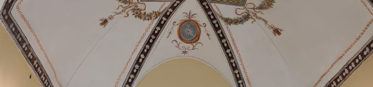 Soffitto elaborato con archi decorativi, motivi floreali e un medaglione centrale su sfondo color crema