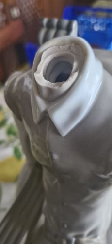 Primo piano di una statuina grigia con colletto bianco e apertura sul collo