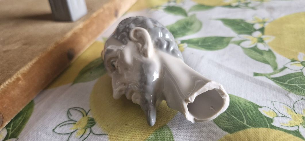 Piccola statuetta bianca a forma di elefante distesa su una tovaglia floreale, con un oggetto di legno accanto