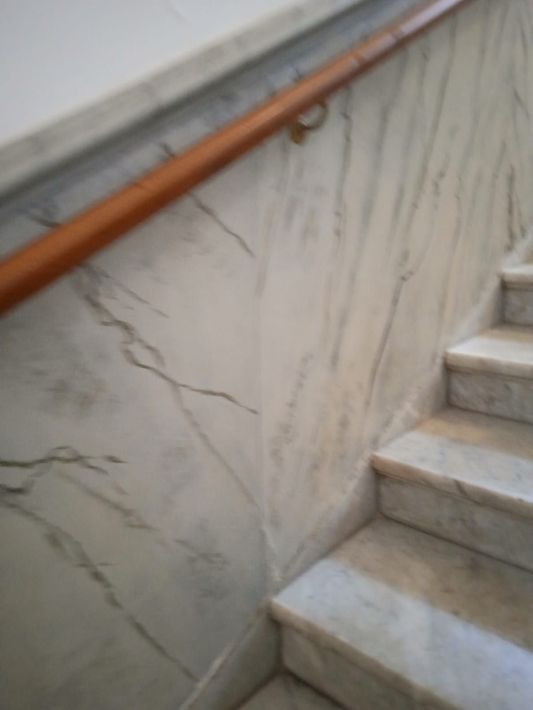 Scala in marmo con corrimano in legno e crepe visibili nei pannelli della parete