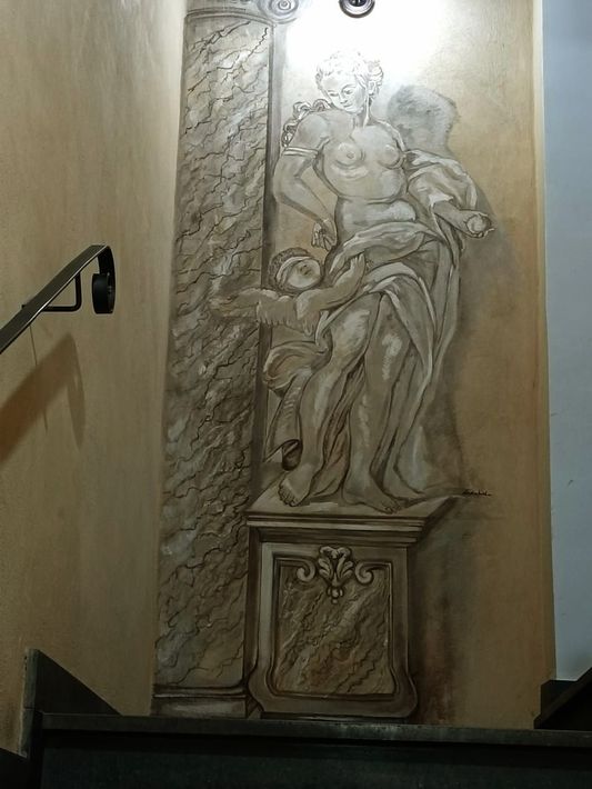 Scultura a rilievo alta e beige raffigurante due figure drappeggiate, in una nicchia di una stretta tromba delle scale
