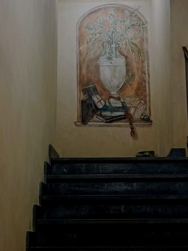 Scala che conduce a un dipinto decorativo raffigurante un vaso, incorniciato e appeso a una parete beige