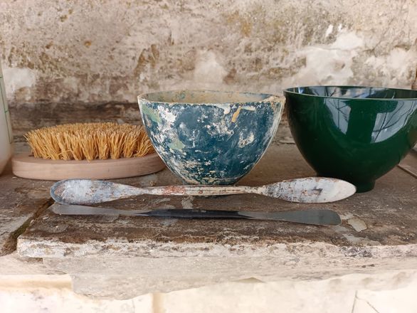 Tre ciotole in ceramica e cucchiai di legno su una mensola di pietra appoggiata a una parete logora