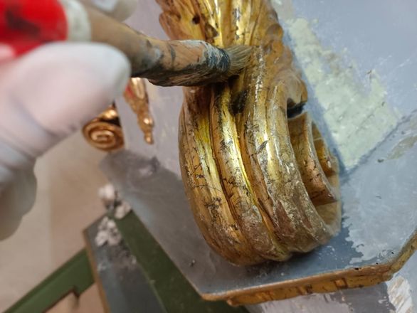 Una mano tiene un piccolo bastoncino di metallo vicino a una cerniera decorata dorata, nell’angolo di una parete