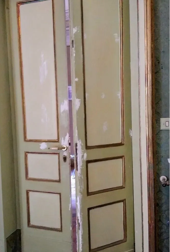 Doppia porta aperta con pannelli color crema e cornice bianca, socchiusa in un corridoio
