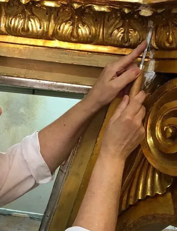 Mani che riparano una cornice decorativa dorata o una modanatura vicino a una finestra