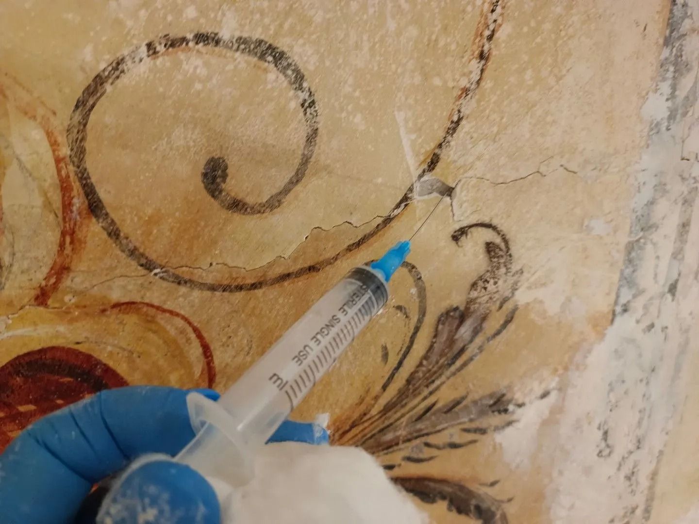 Mano guantata che usa una siringa per iniettare del liquido in una parete dipinta con una tecnica a spirale.
